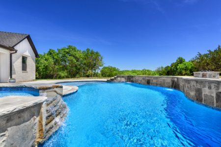 Freeform pool with jacuzzi and wall.