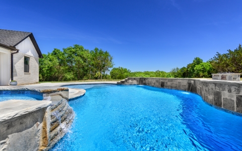Freeform pool with jacuzzi and wall.