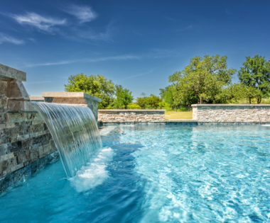 Waterfall into pool, with tree surroundings and blue sky.