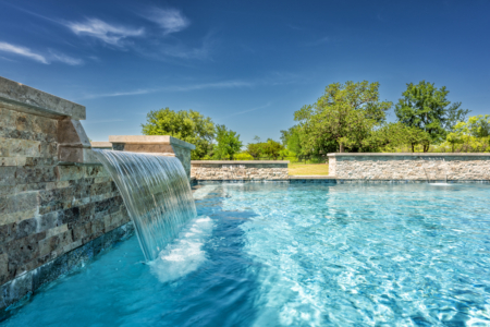 Waterfall into pool, with tree surroundings and blue sky.