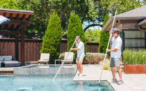 Two pool maintenance guys sweeping pool with net.